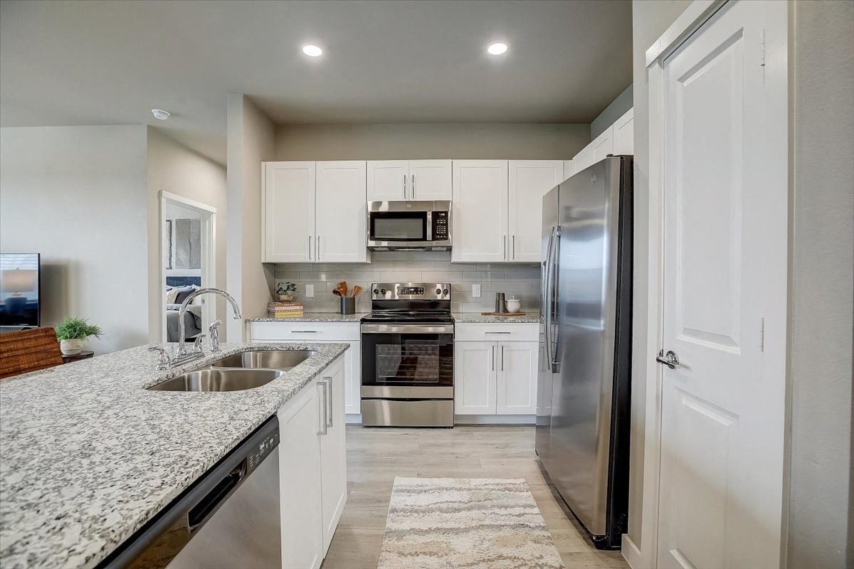 Modern kitchen with island sink, granite countertops, white cabinetry, and stainless steel appliances.